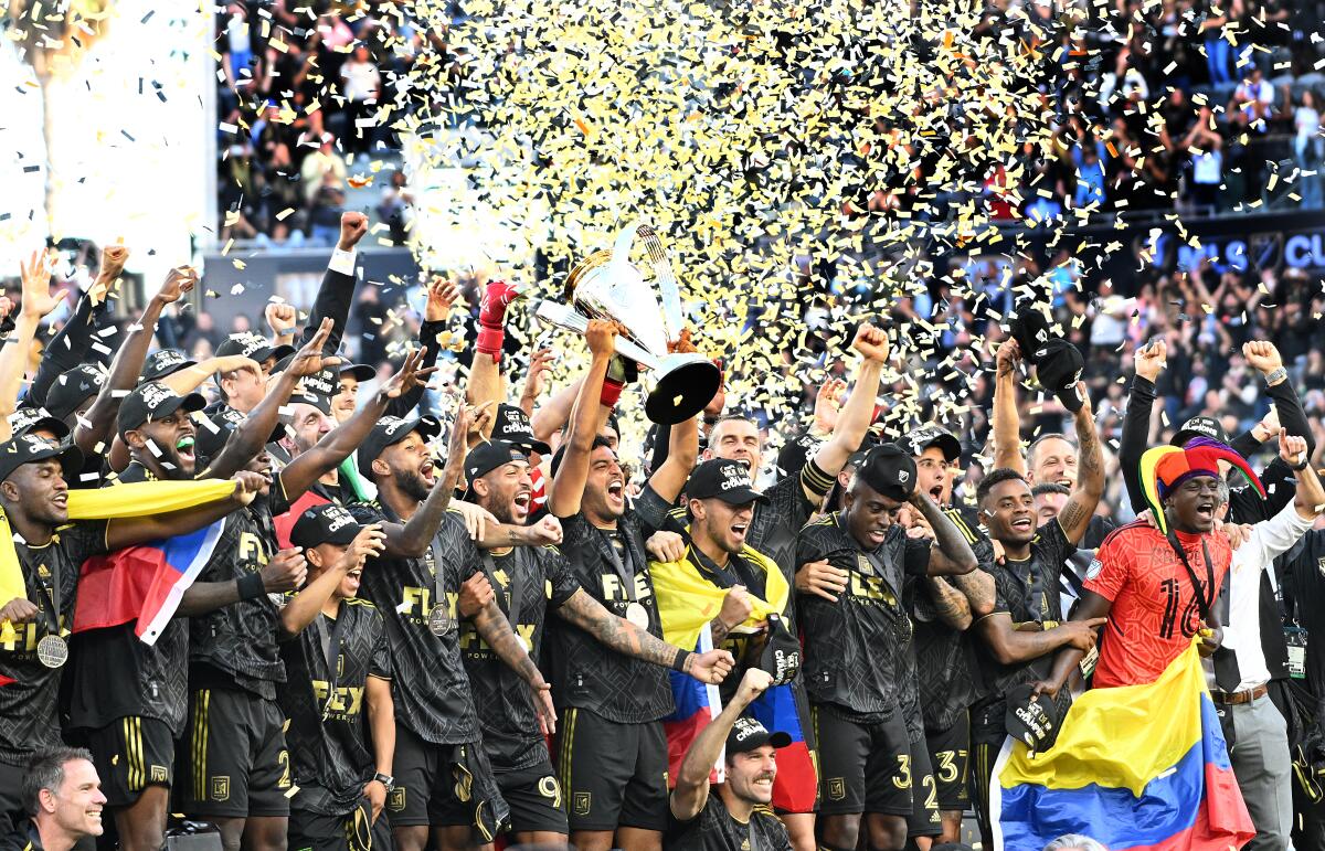 LAFC players celebrate winning the MLS Cup by holding up the trophy as confetti falls