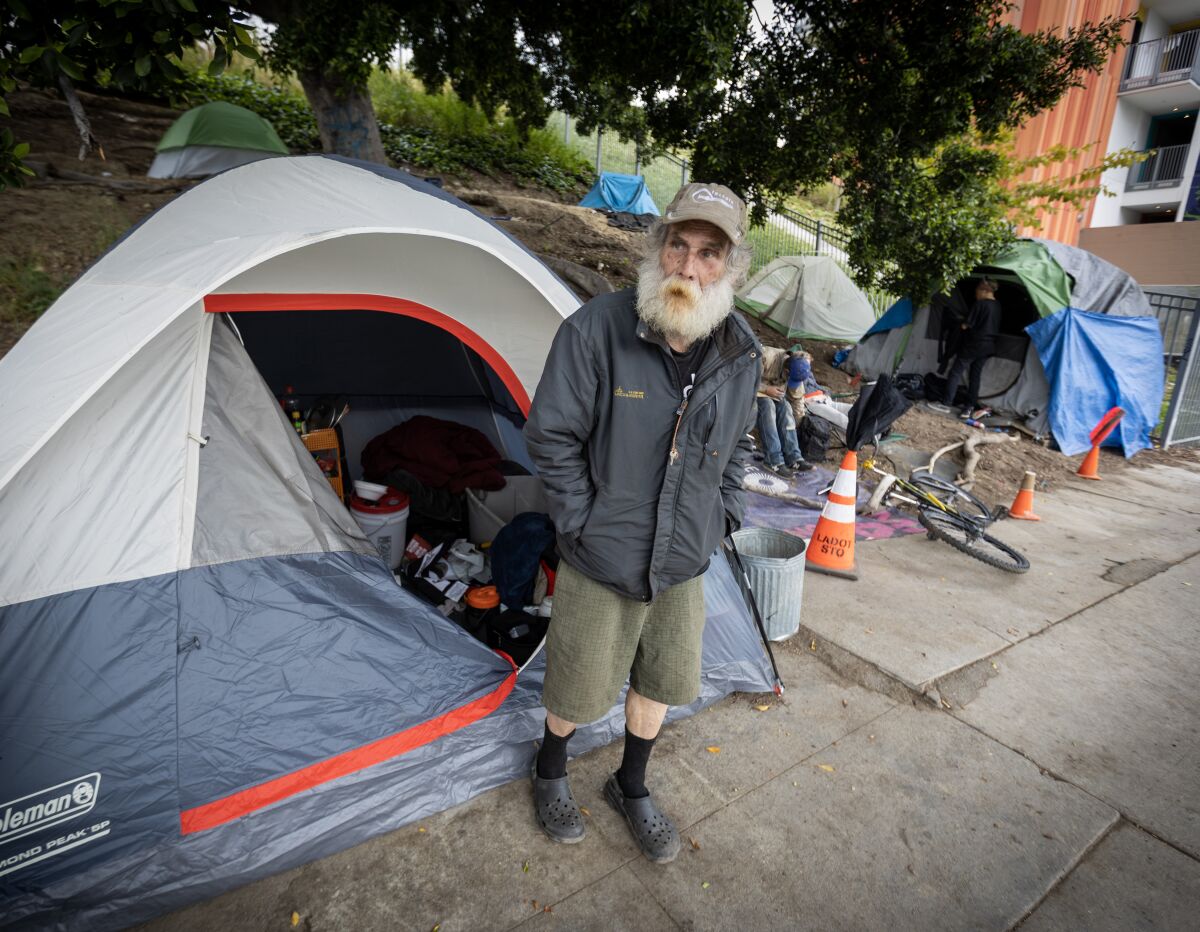A man stands outside a tent on a sidewalk in downtown Los Angeles.
