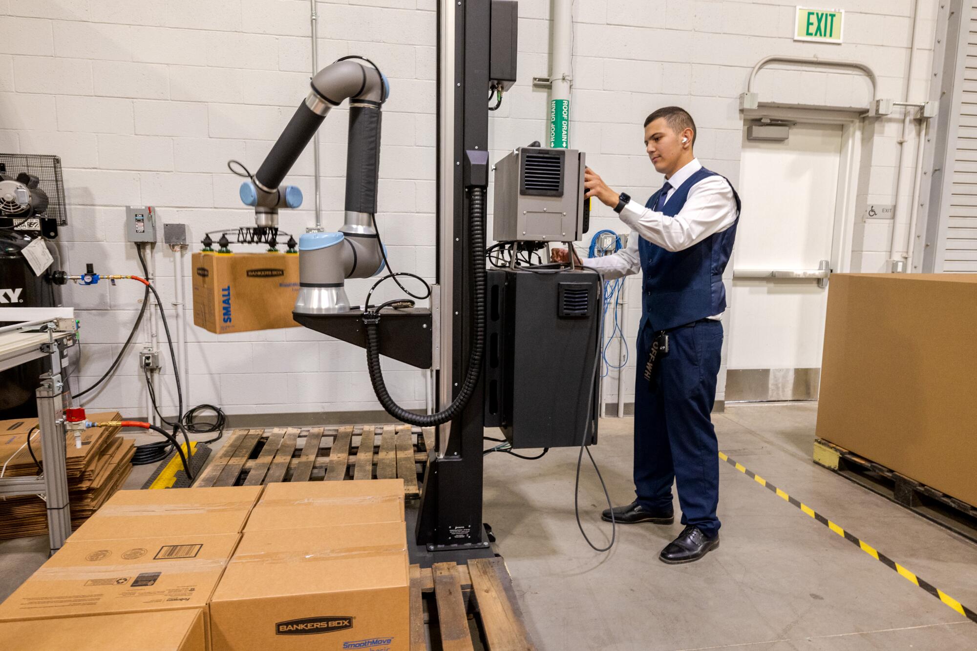 A high school student operates a robotic arm to move packages in a building.