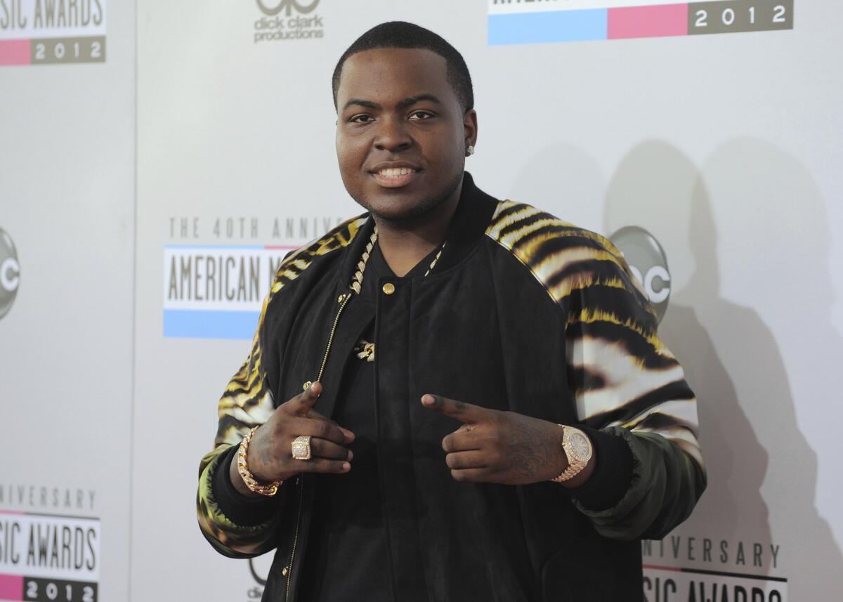 Sean Kingston in a black shirt and a tiger-print jacket pointing with two fingers while posing against a white backdrop