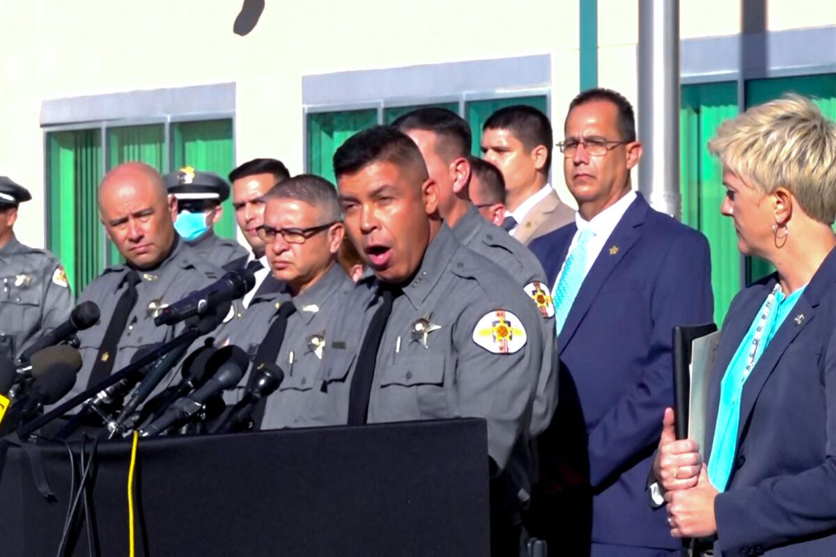 Santa Fe County Sheriff Adan Mendoza at a microphone with other sheriff's deputies and a man and a woman in dark suite.
