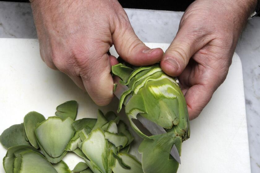 Fill a bowl with cool water and add the juice of 1 lemon. Hold an artichoke in one hand with the stem facing toward you and the tip facing away. Slowly turn the artichoke against the sharp edge of a knife while making an abbreviated sawing motion, cutting the outer leaves at the base.