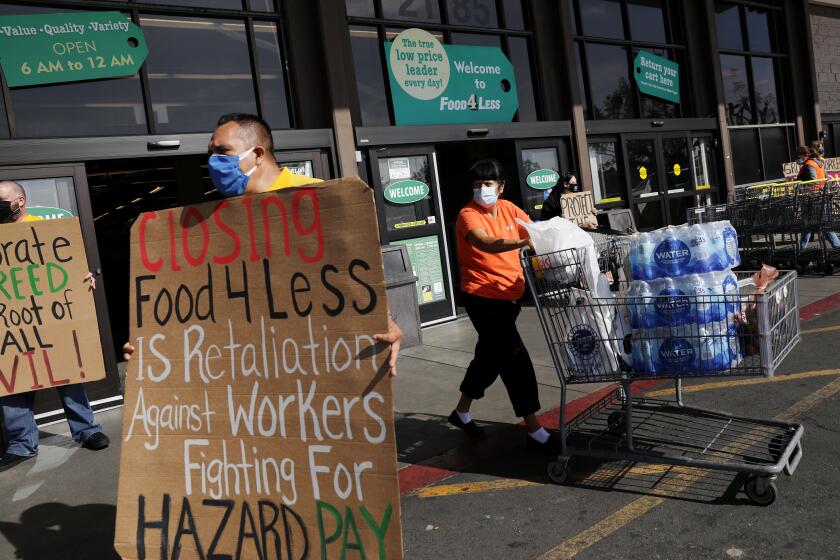 LONG BEACH-CA-FEBRUARY 3, 2021: A shopper passes by a group holding signs in support for Food 4 Less workers at the grocery store on South Street in North Long Beach on Wednesday, February 3, 2021. Food 4 Less workers, city leaders and local labor advocates hold a news conference to call on Kroger Co., the parent company of Food 4 Less and Ralph's, to keep stores open and condemn the company's actions to close two of its locations in the city because of the city's emergency ordinance for $4 per hour in temporary hazard pay. (Christina House / Los Angeles Times)