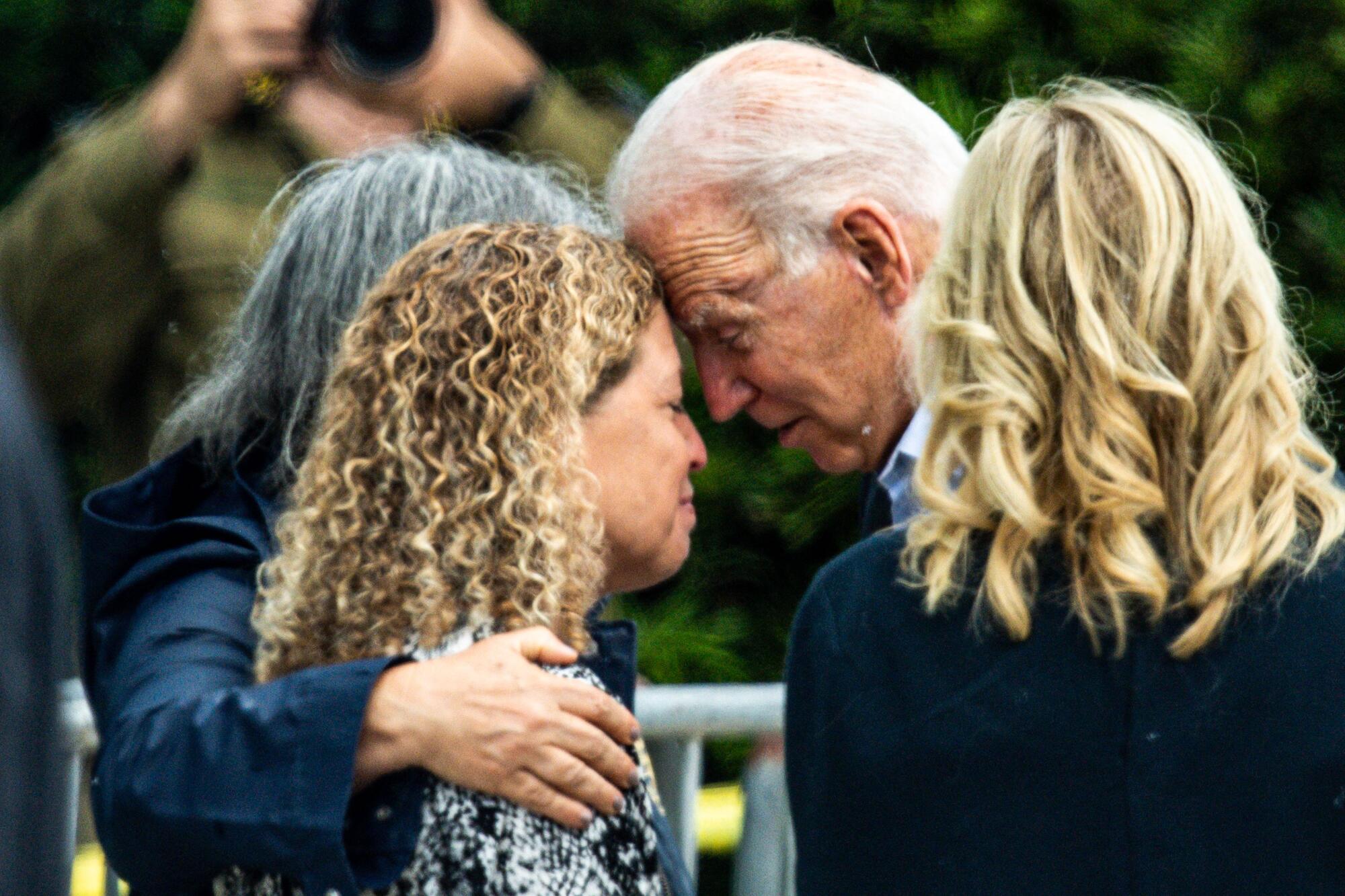 Biden leans his forehead against the forehead of an emotional woman.