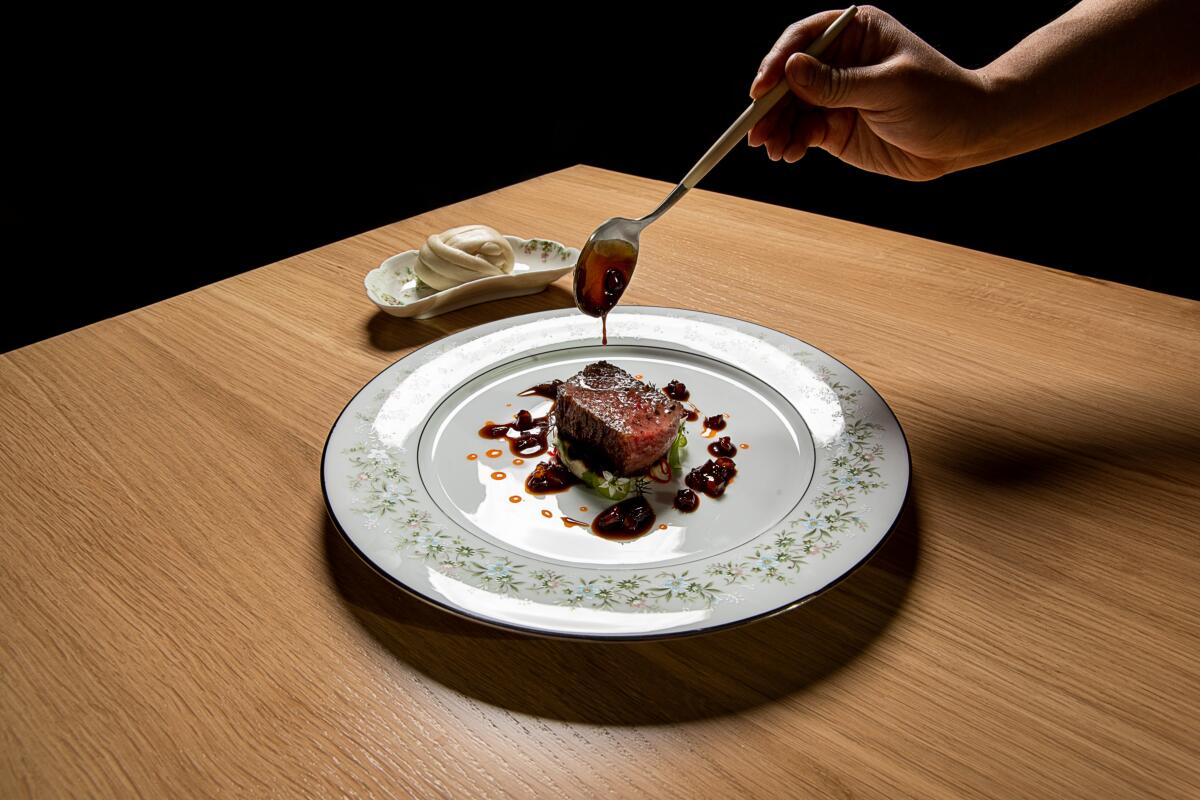 A photo of a hand dripping black-garlic sauce onto a strip of beef. 
