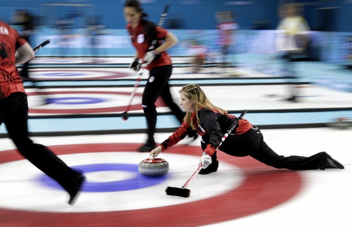 Canada's skip Jennifer Jones, right, delivers the rock while teammates Jill Officer, center, and Dawn McEwen, left, prepare to sweep.
