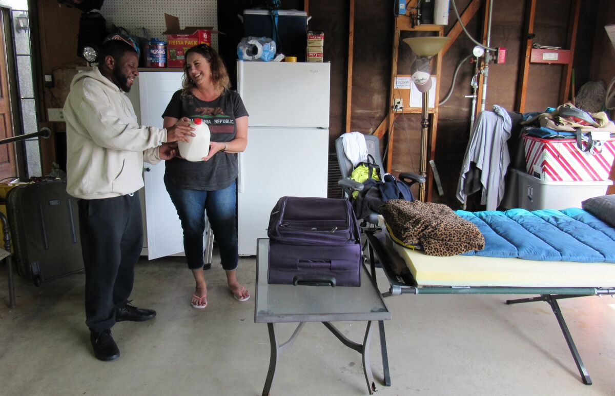 Walter Johnson IV and Aimee Morrison laugh over a joke about spoiled milk in the garage of a Home of Guiding Hands group home in Lakeside. The two are part of a self-imposed quarantining effort meant to keep six developmentally challenged clients safe during the coronavirus pandemic.