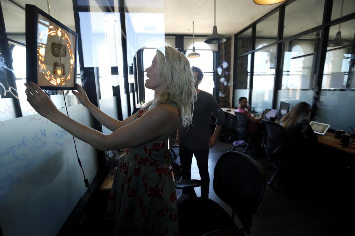 Pamela Fox, Woebot's chief technology officer, hangs a picture frame that contains the logo for the start-up as others work in their San Francisco office.