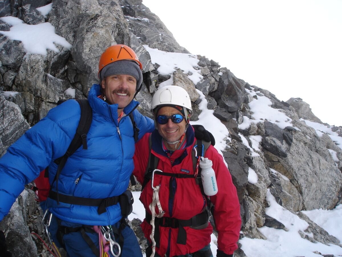 Two men in climbing gear stand on a rocky, icy mountain