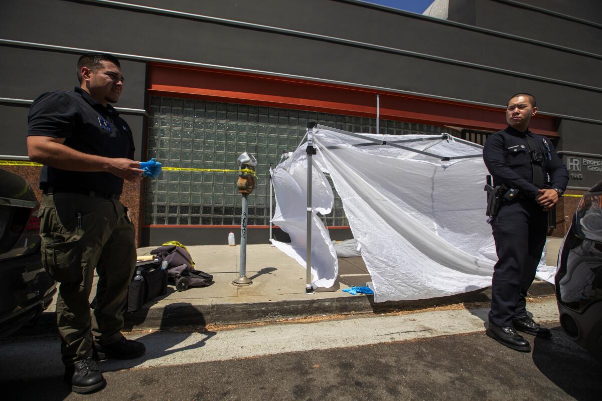 Coroner's investigator Adrian Munoz, left, prepares to examine and remove the body of Alvin Robinson in West Los Angeles.