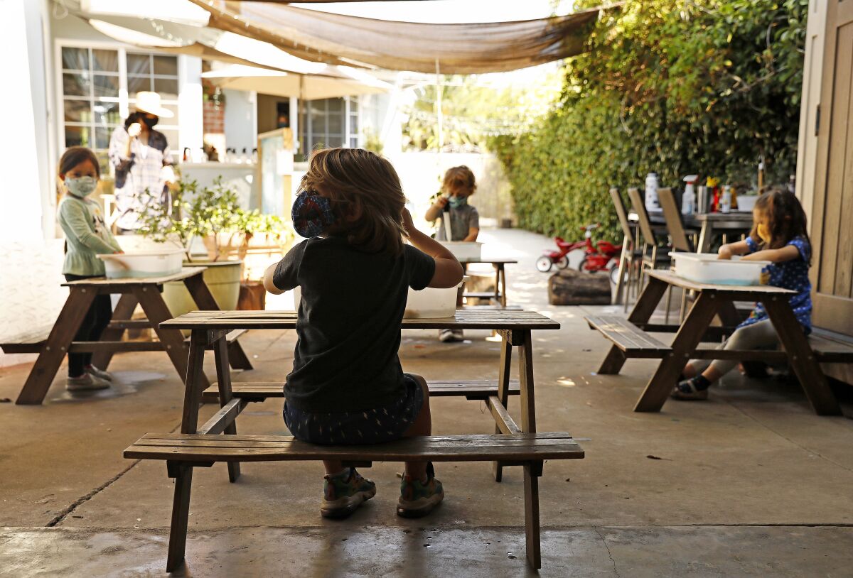 Children do activities outside at separate tables at Voyages Preschool in Los Angeles.