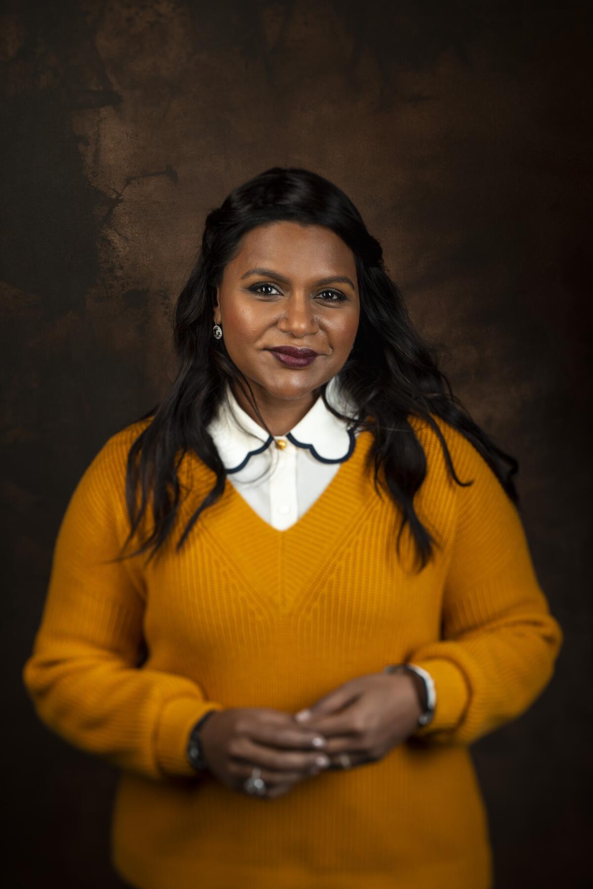 A woman with long, black hair posing in an orange sweater