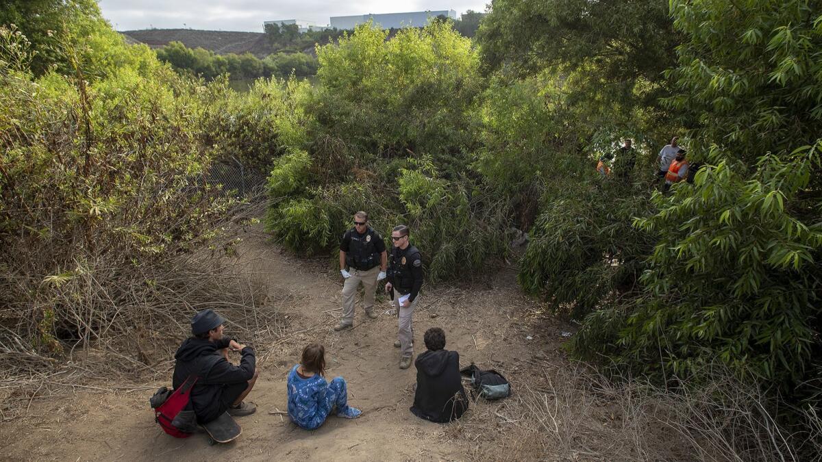 Officers Gabe Ricci, left, and Daniel Chichester of the Huntington Beach Homeless Task Force talk with homeless people near an encampment off Ellis Avenue.