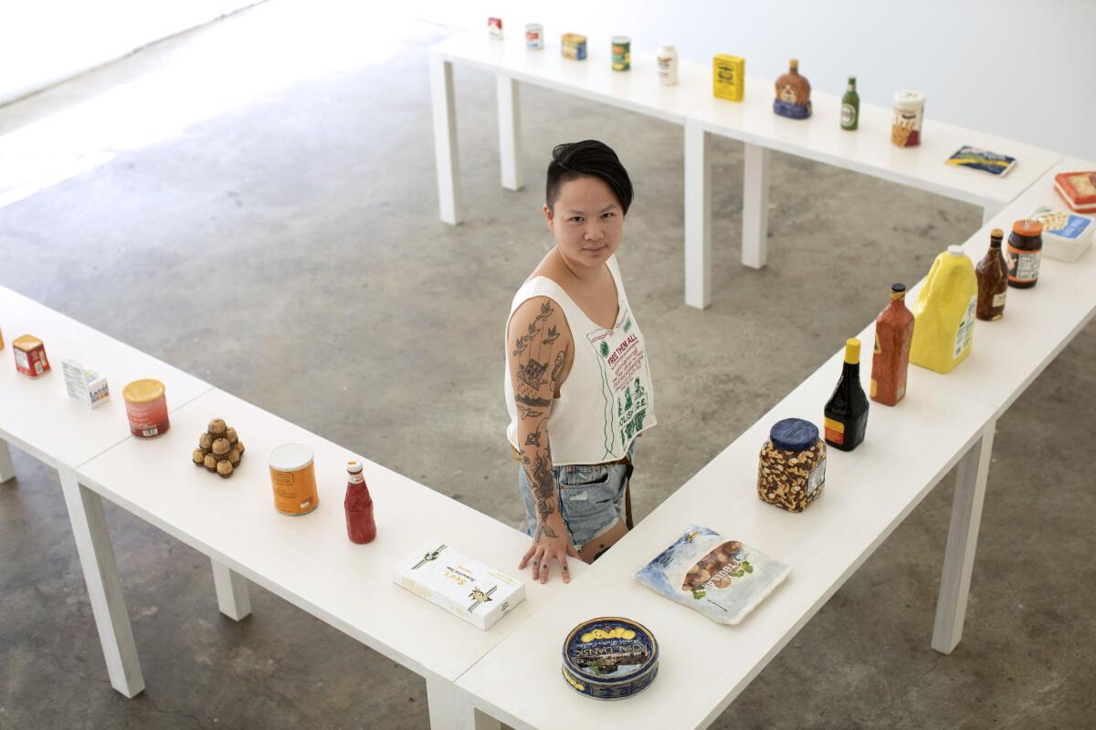An artist stands surrounded by clay pieces she created to represent food products such as Spam and ketchup.