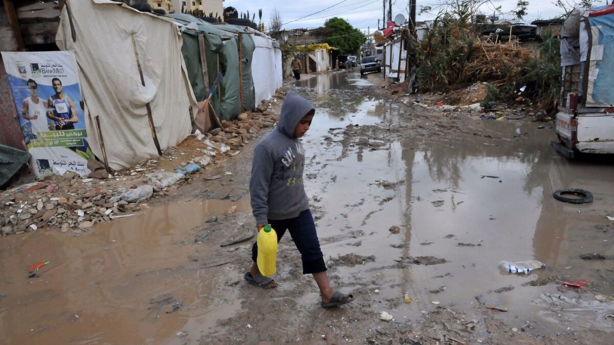 A Syrian refugee boy walks in a muddy alley at a makeshift camp near the northern city of Tripoli, Lebanon, in 2013.