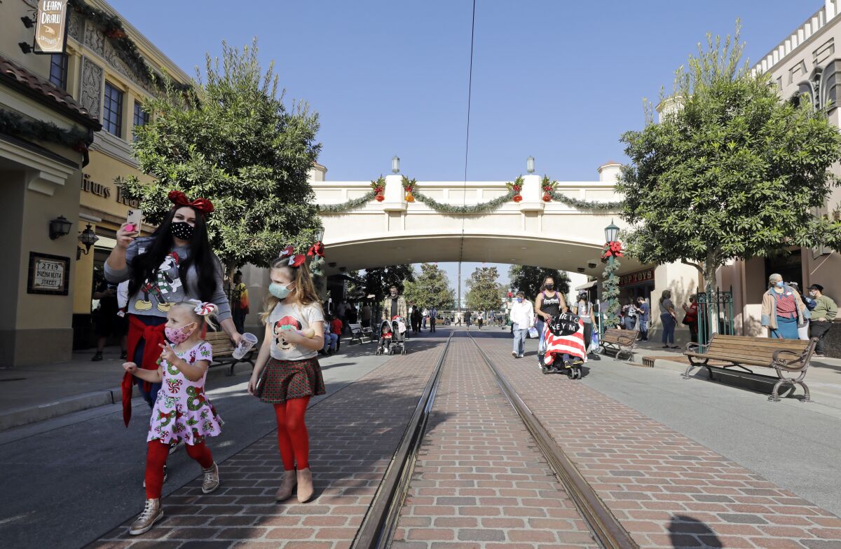 A few masked adults and children on Buena Vista Street at Disney California Adventure.
