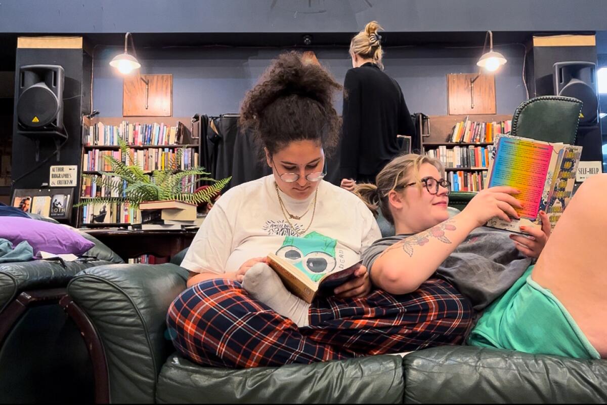 Two people sit next to each other on a couch in a bookstore.