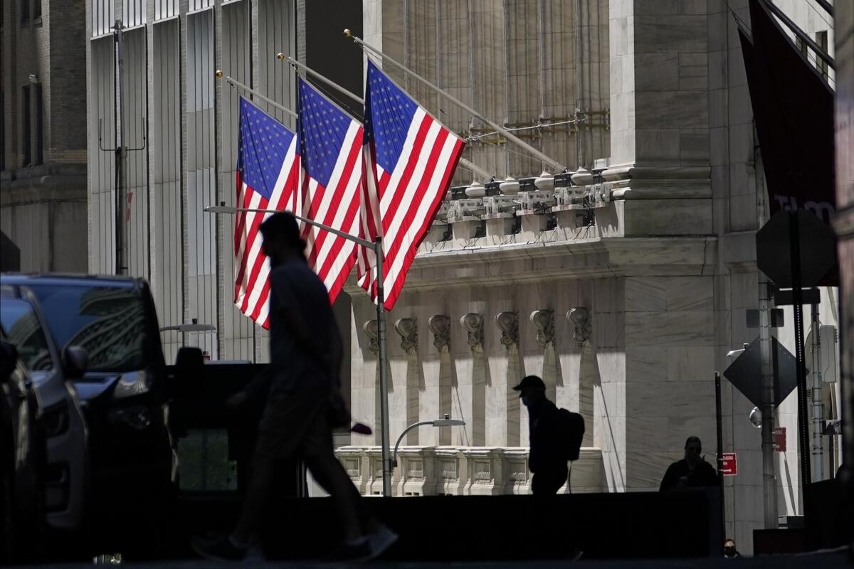 Pedestrians pass the New York Stock Exchange, which has three U.S. flags hanging from it.