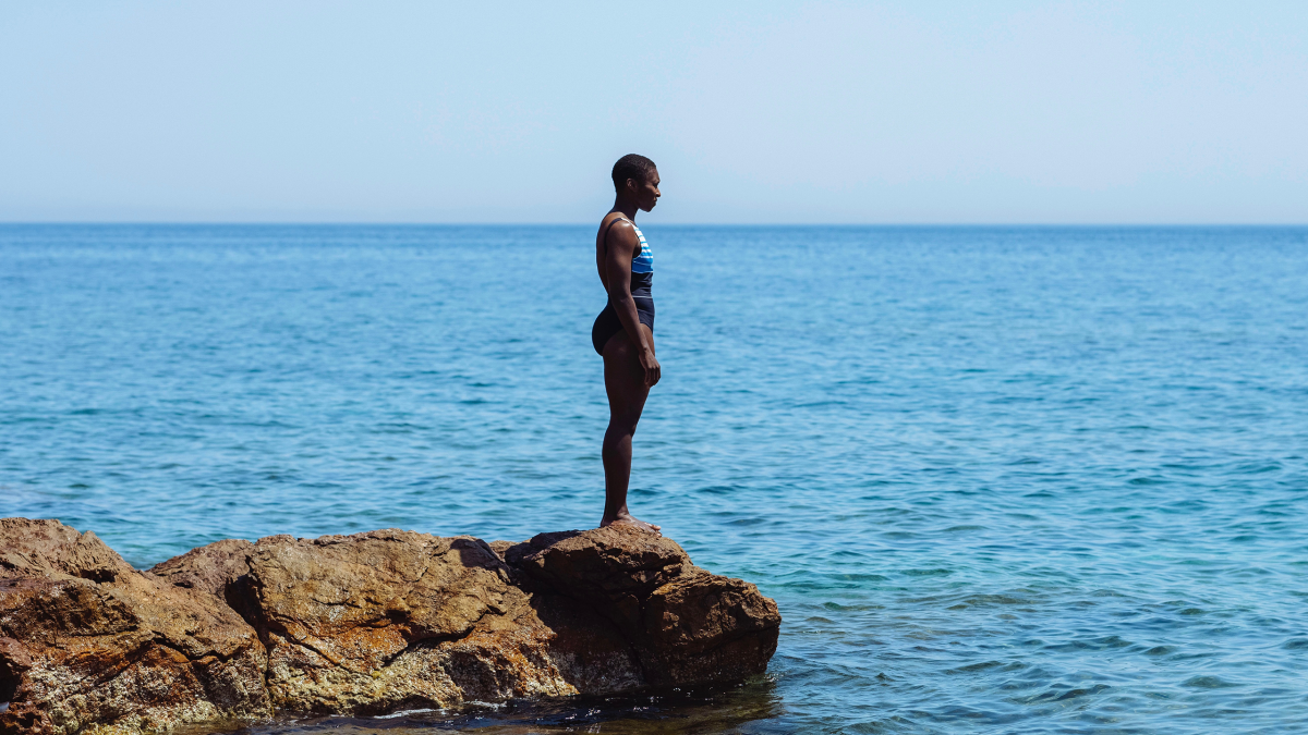 A woman in a swimsuit stands on rocks by the sea