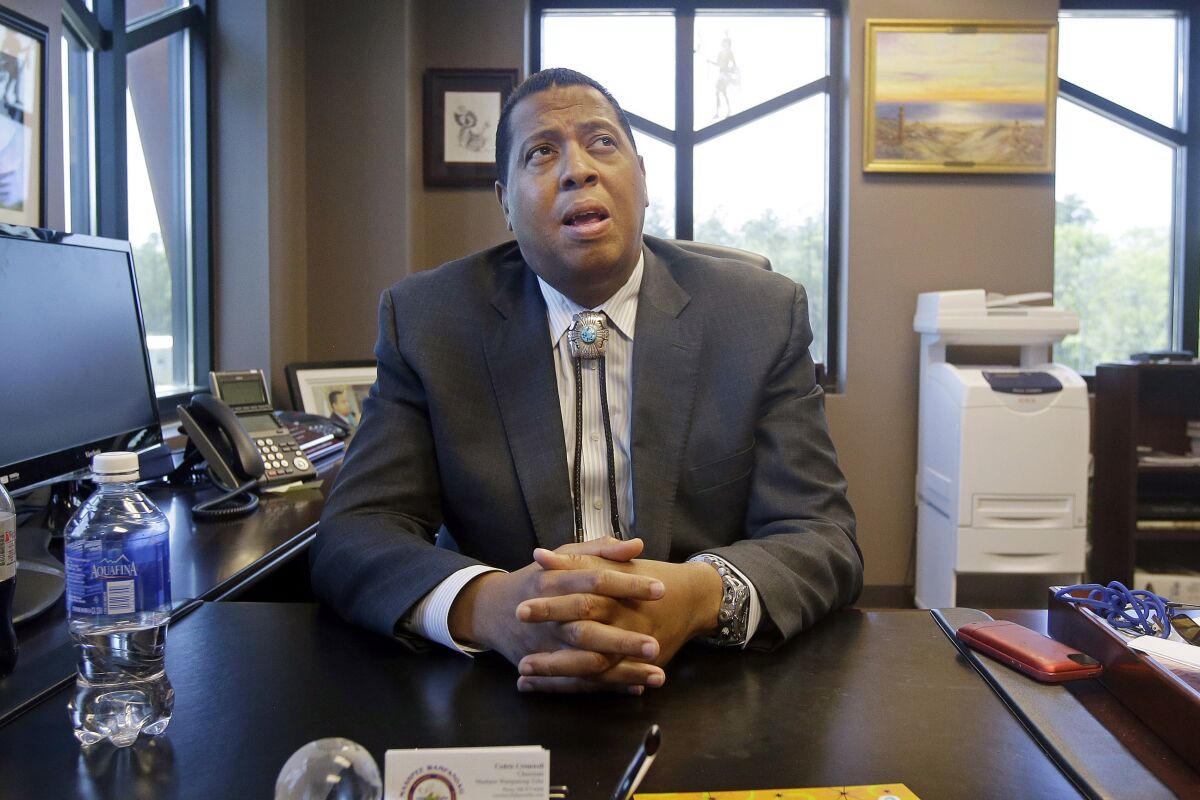FILE - In this May 29, 2014 photo, Mashpee Wampanoag Tribe Chairman Cedric Cromwell sits behind his desk at the government center in Mashpee, Mass. Cromwell and the owner of a Rhode Island architecture firm were arrested Friday, Nov. 13, 2020, and charged in a bribery scheme involving the tribe's plans to build a resort casino in Taunton, Mass. (AP Photo/Stephan Savoia, File)