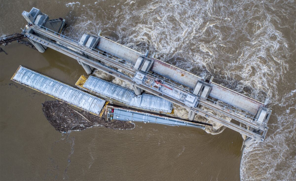 Two barges are stuck against the dam just south of downtown Louisville, Ky., on Tuesday, March 28, 2023. Crews were working Wednesday to remove three remaining barges that got loose on the Ohio River, including one carrying methanol. (Michael Clevenger/Courier Journal via AP)
