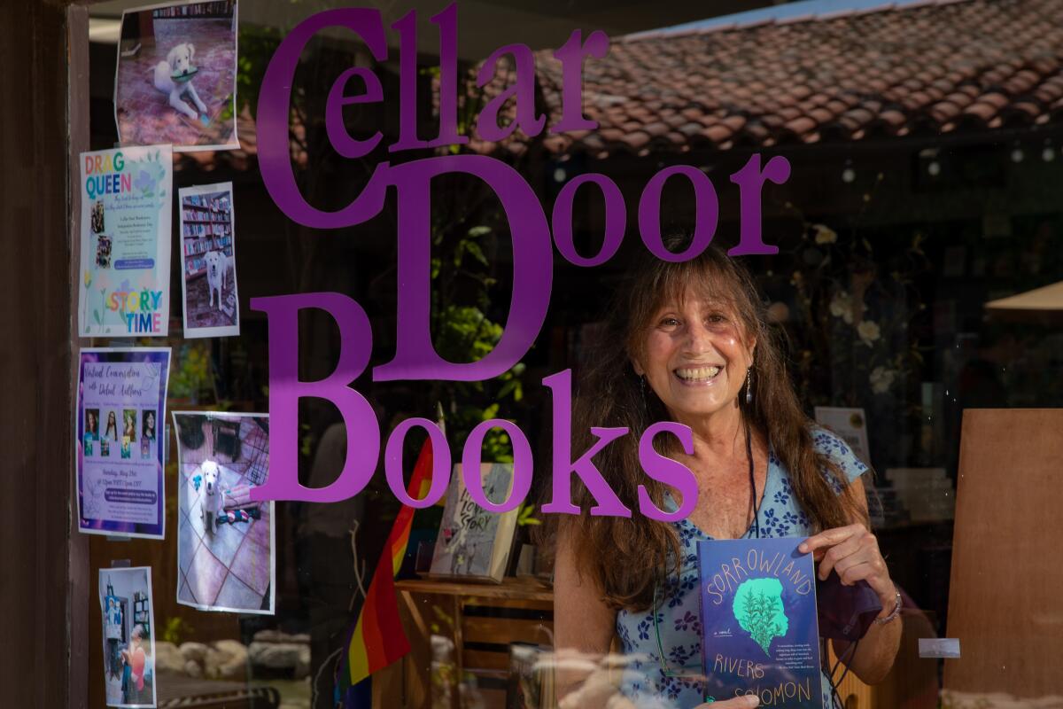 A middle aged woman stands behind a window reading "Cellar Door Books."