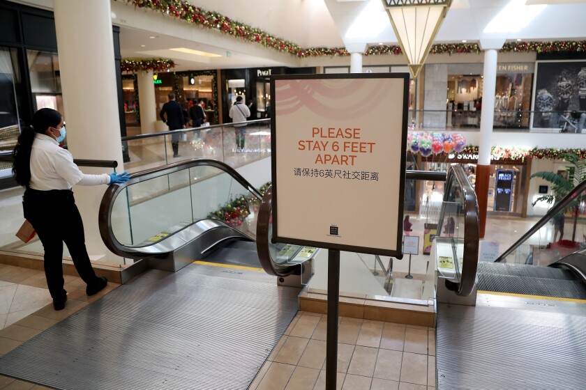 A custodian uses a wipe to sanitize an escalator handrail during Black Friday at South Coast Plaza.