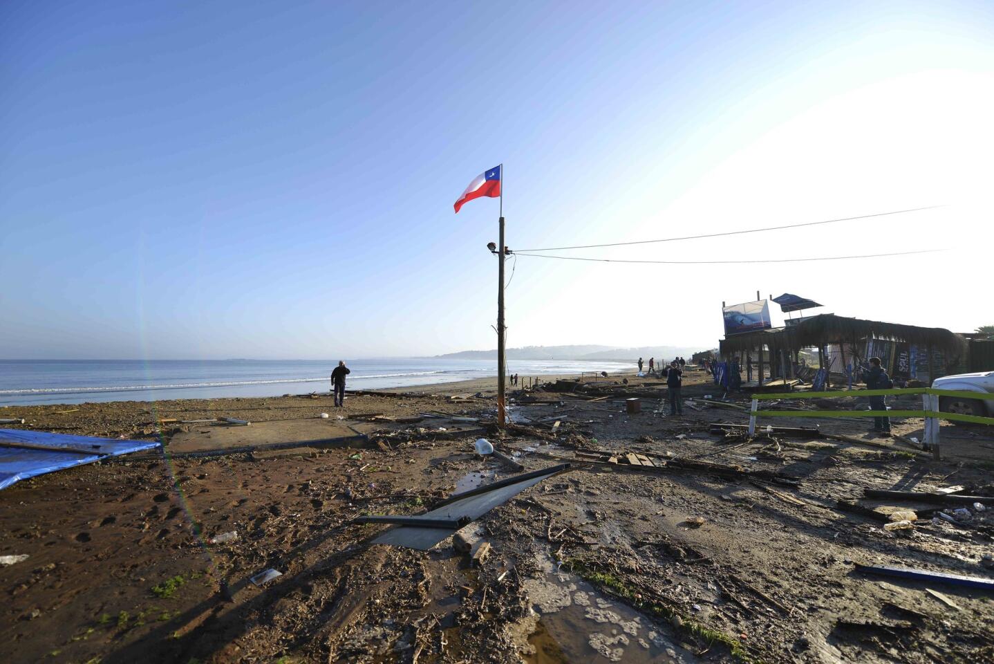 A man walks past a lone Chilean flag where surfing schools once stood, swept away by an earthquake-triggered tsunami in Concon, Chile.