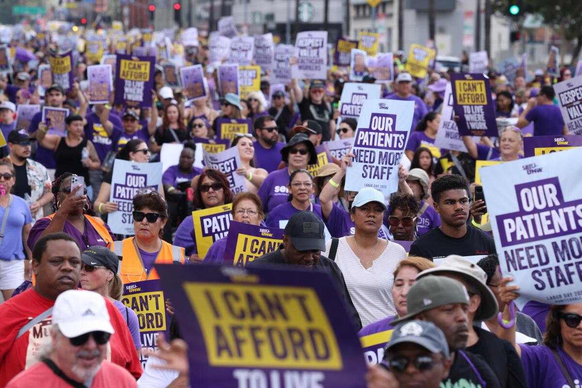 People hold signs reading "Our patients need more staff" and "I can't afford to live where I work."