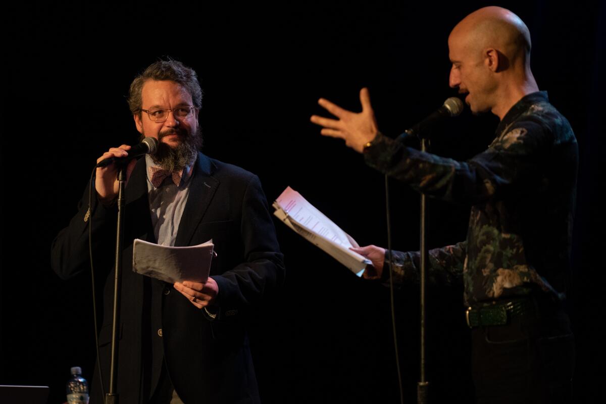 Two men stand at microphones.