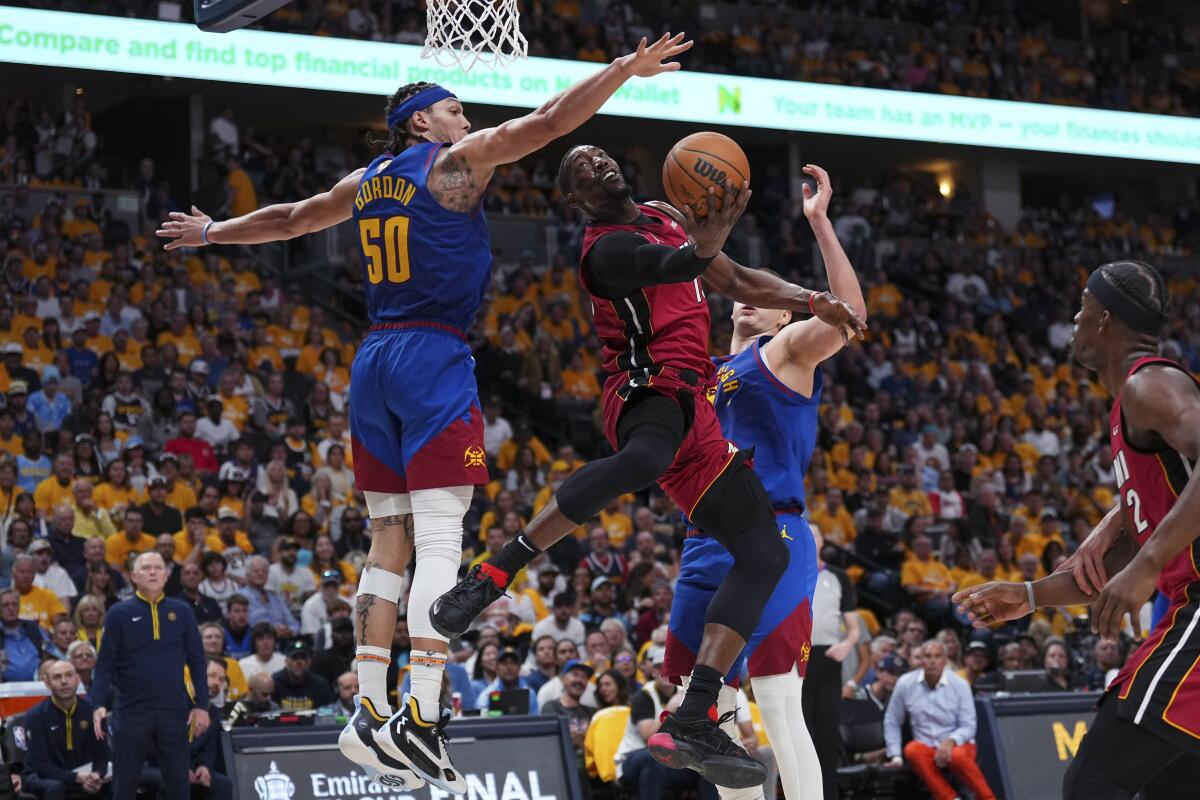 Miami Heat center Bam Adebayo shoots while defended by Denver Nuggets forward Aaron Gordon and center Nikola Jokic.
