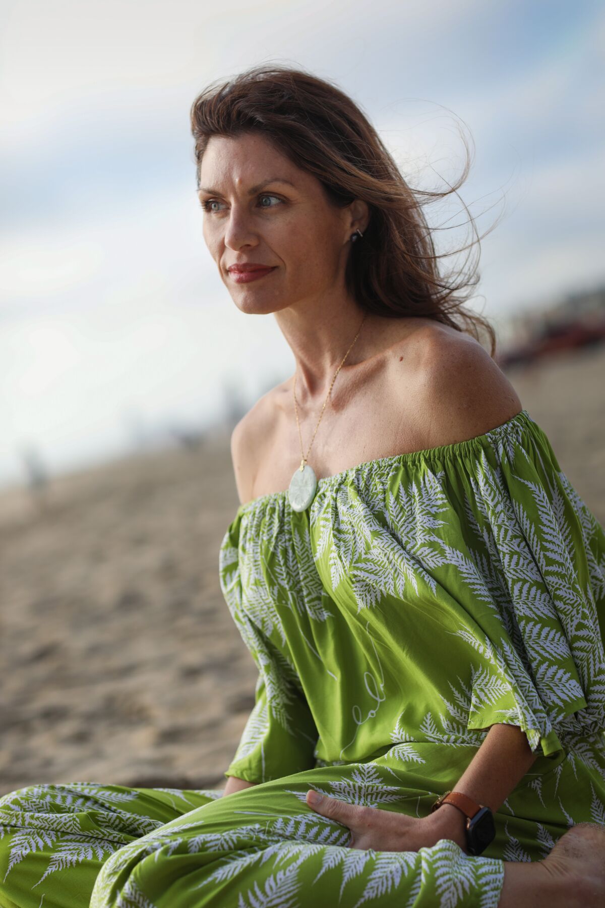 A woman in a green strapless dress sitting on the beach.