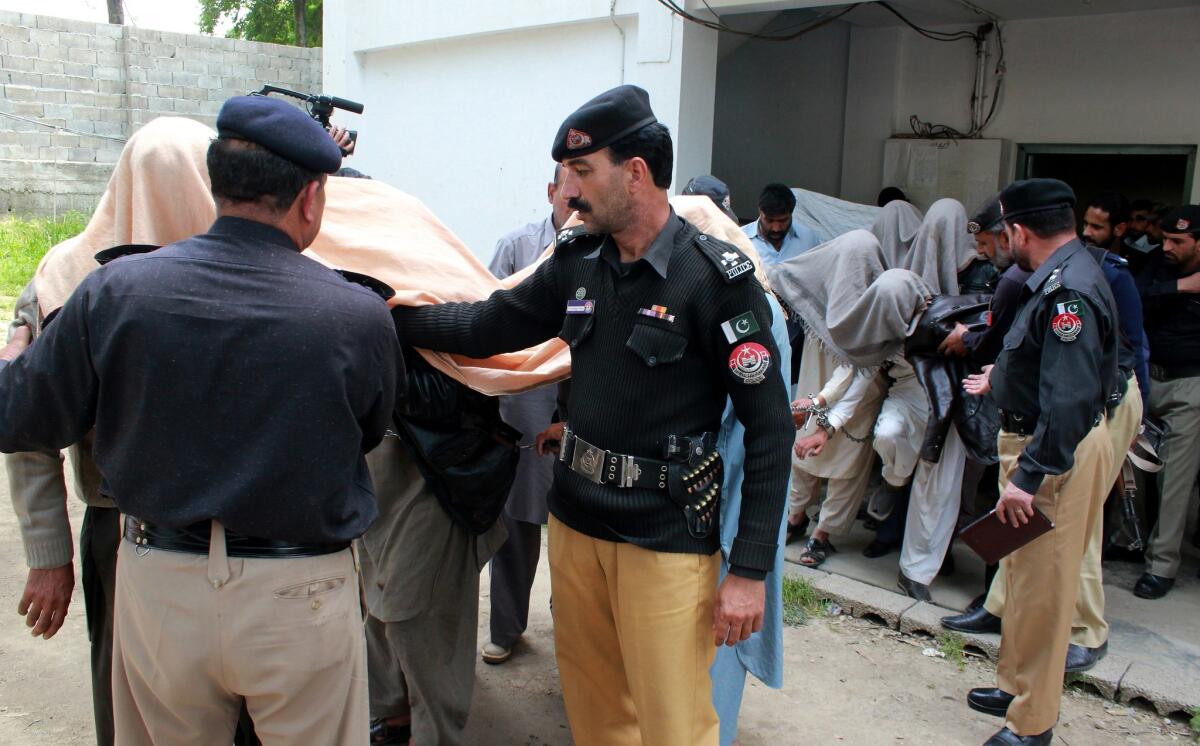 Pakistani police escort members of a local tribal council, with their faces covered, outside a court in Abbottabad after the death and burning of a girl.