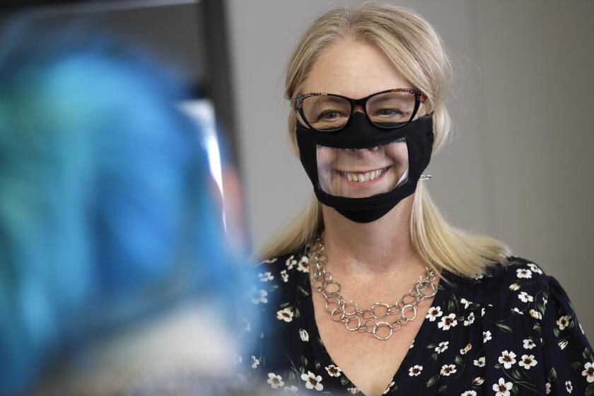 In this June 3, 2020, photo, Chris LaZich, of Fleet Science Center, wears a mask with a window as she talks with Delpha Hanson in San Diego. Face coverings to curb the spread of the coronavirus are making it hard for people who read lips to communicate. That has spurred a slew of startups making masks with plastic windows to show one's mouth. The companies are getting inundated with orders from family and friends of deaf people, people helping English learners see the pronunciation of words, and even hospitals that want their patients to be able to see smiles. (AP Photo/Gregory Bull)