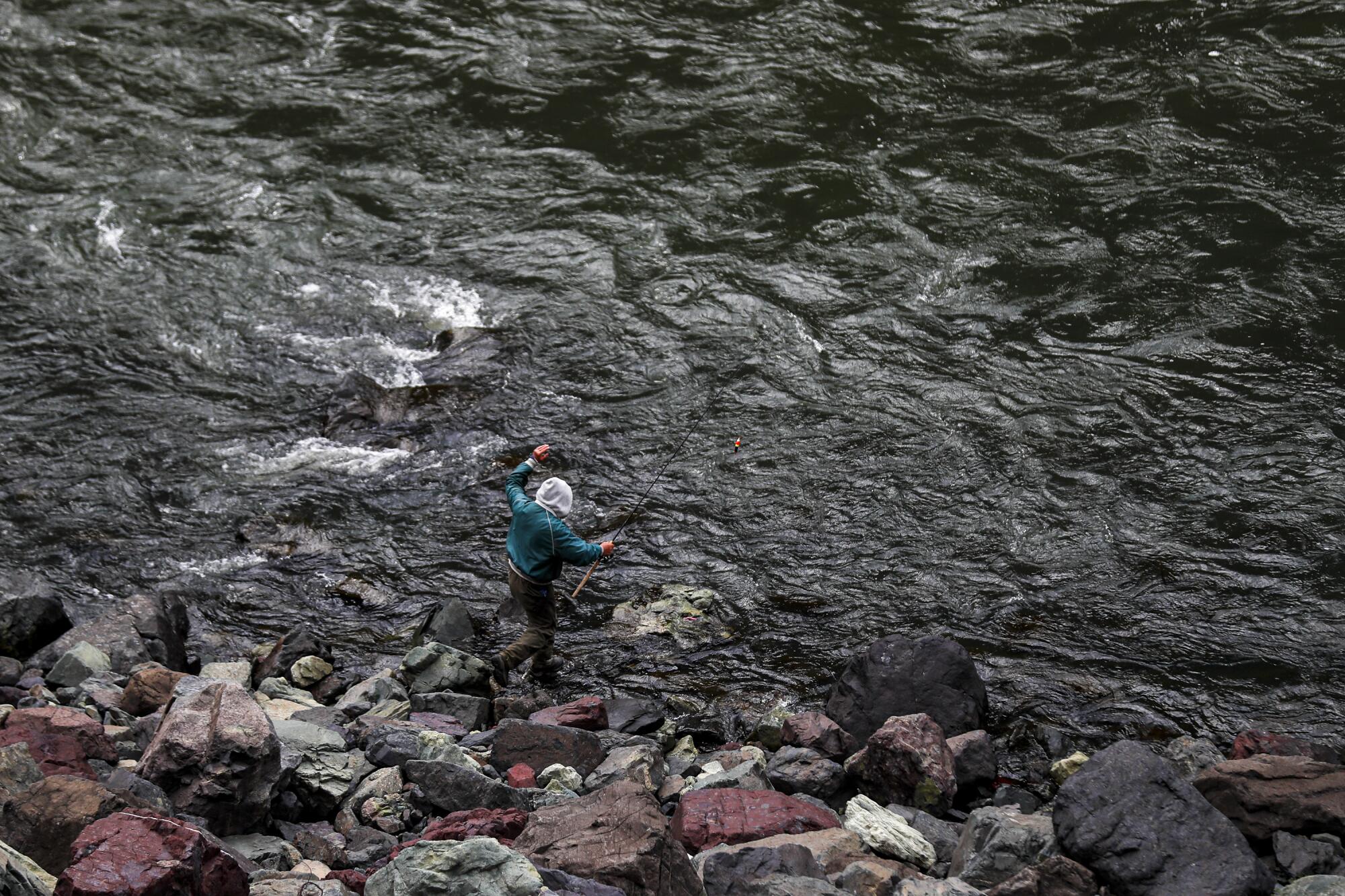 A person fishes on the rocky shoreline of the Snake River near Hells Canyon Dam.