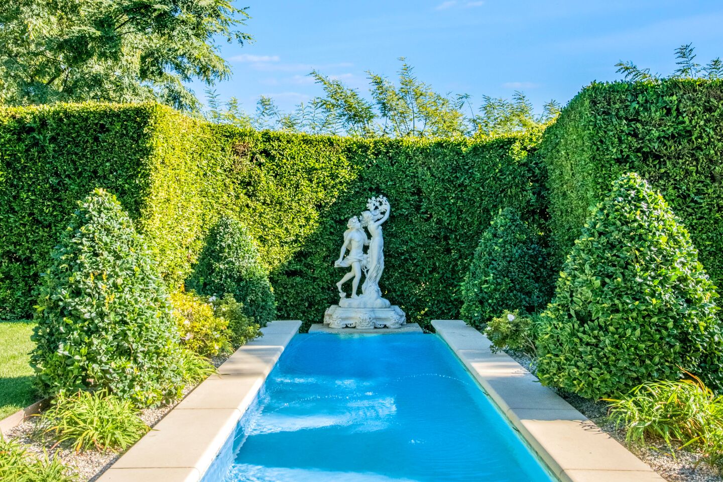 The long rectangular reflecting pool has a statue at one end and tall hedges.