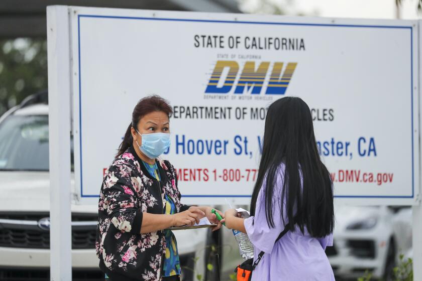 WESTMINSTER, CA - AUGUST 13: DMV staffer Kathy Cao, left, distributes numbers among the people lined up for DMV to open on Thursday, Aug. 13, 2020 in Westminster, CA. (Irfan Khan / Los Angeles Times)