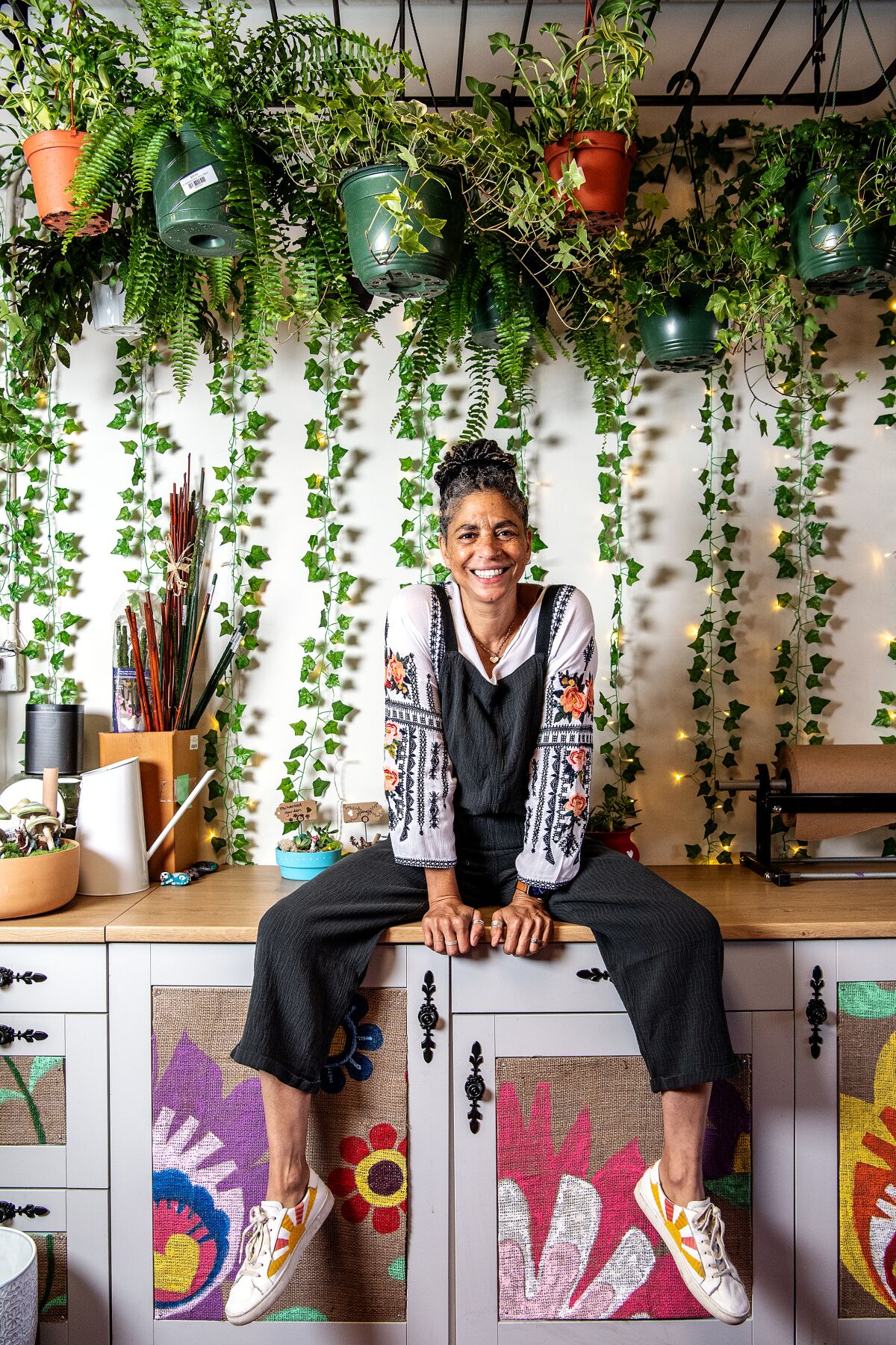 Photograph of Shawna Christian, sitting on a counter under hanging plants