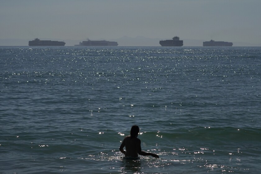 Man wading in ocean with container ships in the distance