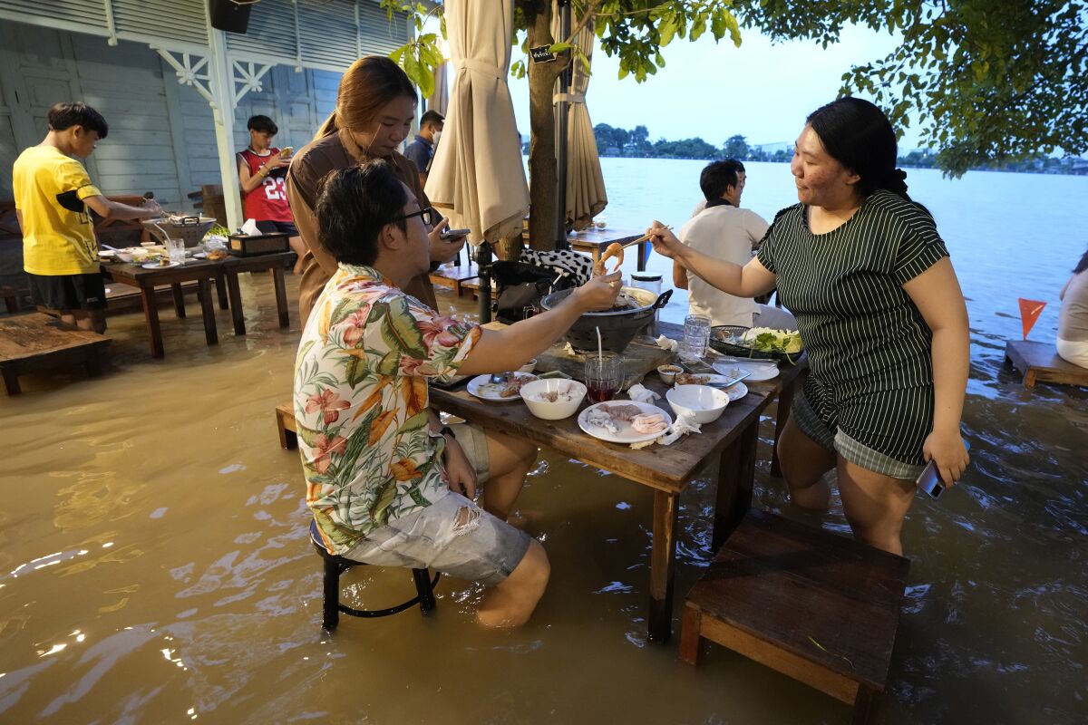 Customers of the riverside Chaopraya Antique Café enjoy themselves despite the extraordinary high water levels in the Chao Phraya River in Nonthaburi, near Bangkok, Thailand, Thursday, Oct. 7, 2021. The flood-hit restaurant has become an unlikely dining hotspot after fun-loving foodies began flocking to its water-logged deck to eat amid the lapping tide. Now, instead of empty chairs and vacant tables the “Chaopraya Antique Café” is as full as ever, offering an experience the canny owner has re-branded as “hot-pot surfing.” (AP Photo/Sakchai Lalit)