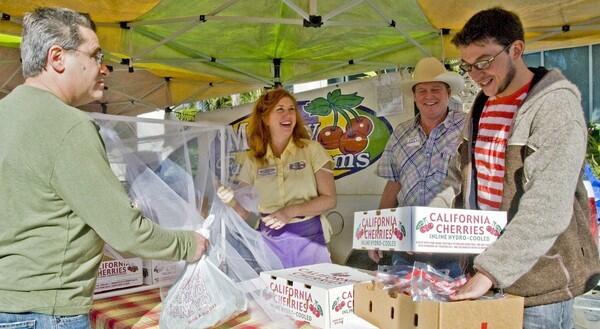 Steven and Vickie Murray of Murray Family Farms, in Arvin, sell Sequoia brand cherries, varieties that are very good early-season fruits, at the Santa Monica farmers market. At right, Sassan Rostamian, owner and chef of Sauce on Hampton restaurant in Venice, buys a box of cherries.