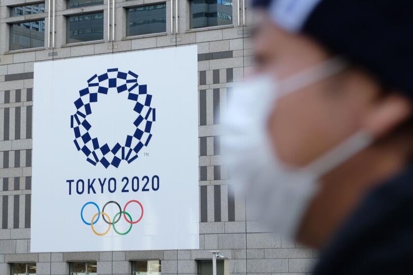 A man wearing a mask passes the logo of the Tokyo 2020 Olympic Games displayed on the Tokyo Metropolitan Government building on March 19, 2020. (Photo by Kazuhiro NOGI / AFP) (Photo by KAZUHIRO NOGI/AFP via Getty Images)