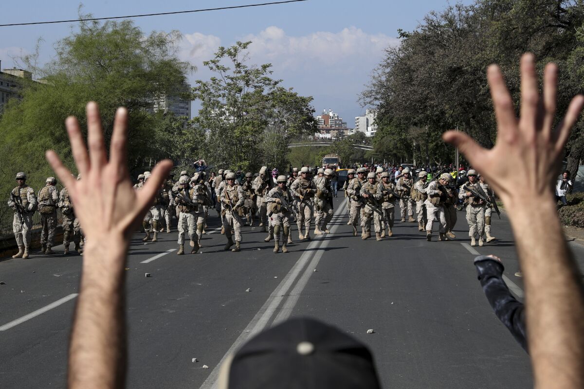 A demonstrator holds up his hands toward advancing soldiers during a protest as a state of emergency remains in effect in Santiago, Chile, Sunday, Oct. 20, 2019. Protests in the country have spilled over into a new day, even after President Sebastian Pinera cancelled the subway fare hike that prompted massive and violent demonstrations.