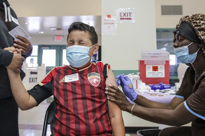 Los Angeles , CA - May 14: Christiana Neri, 38, holds her 13-year-old son Ivan Hernandez as Sequoia Hutton administers Pfizer COVID-19 vaccine at a mobile vaccine clinic held for age 12 and over at Roosevelt Park on Friday, May 14, 2021 in Los Angeles , CA. (Irfan Khan / Los Angeles Times)