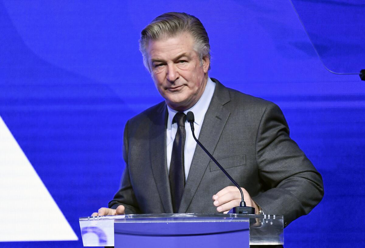 Alec Baldwin at a lectern, against a blue background
