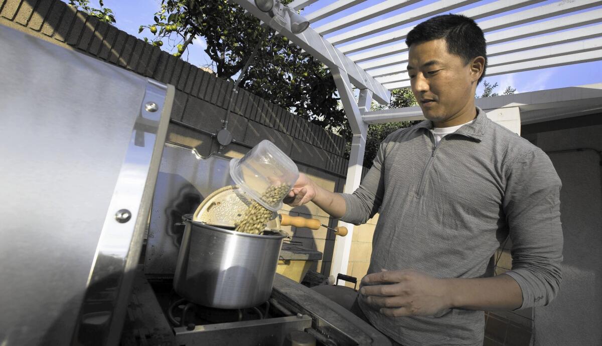 Los Angeles Times reporter Jason Song pours green coffee beans in a popcorn popper to roast on his patio BBQ grill at his home in South Pasadena.