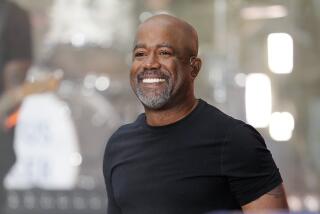 Darius Rucker wears a black t-shirt and smiles onstage