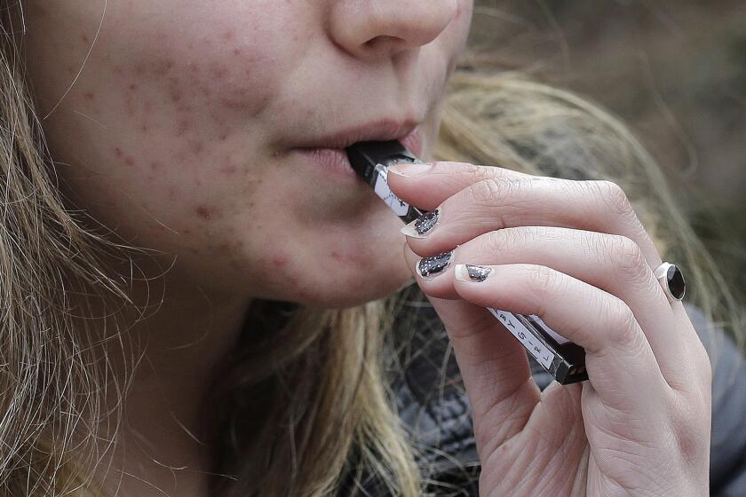 FILE - In this April 11, 2018, file photo, a high school student uses a vaping device near a school campus in Cambridge, Mass. The Trump administration announced Thursday that it will prohibit fruit, candy, mint and dessert flavors from small, cartridge-based e-cigarettes that are popular with high school students. But menthol and tobacco-flavored e-cigarettes will be allowed to remain on the market. (AP Photo/Steven Senne, File)