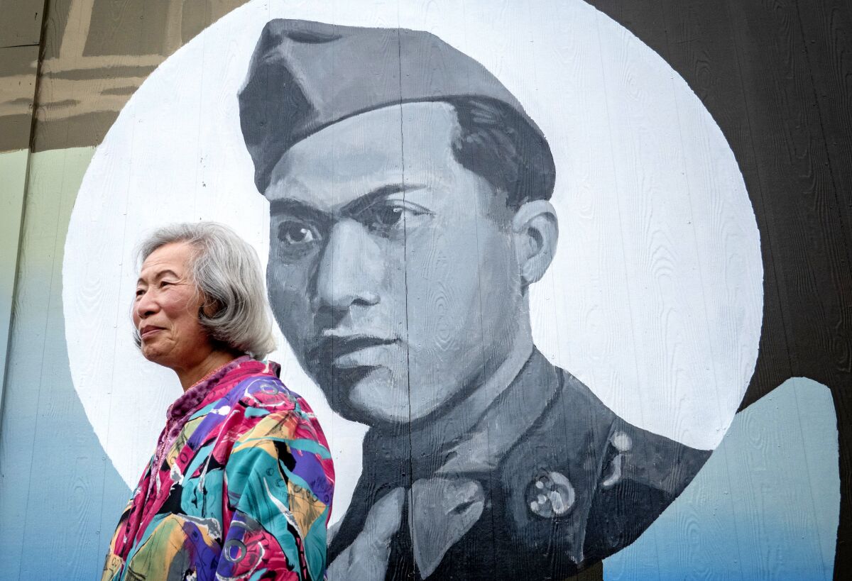 A woman stands in front of a mural of a man in military uniform.