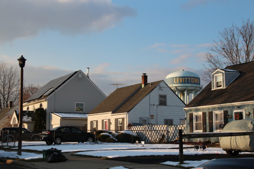 Small residential houses with snow in the yards in front of a water tower with the word Levittown